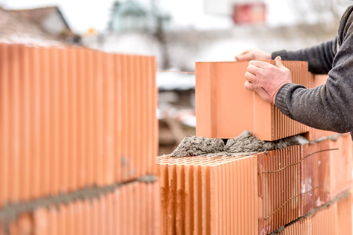 Chantier de construction extérieur avec maçon posant des briques en terre cuite rouge sur un mur