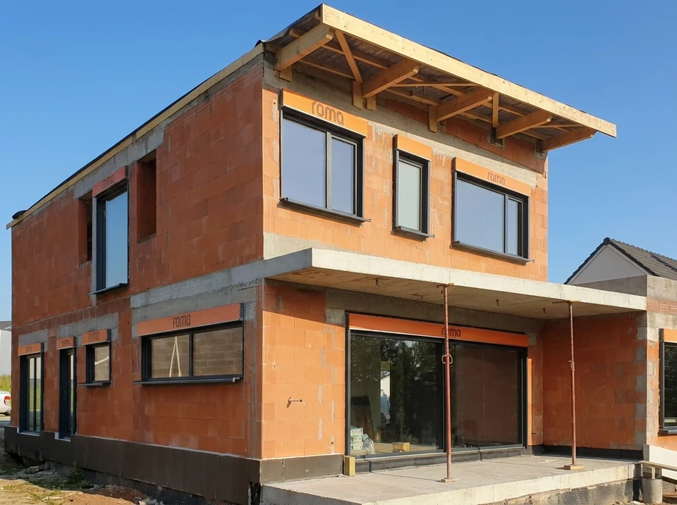 Maison individuelle moderne en construction avec toit à deux pans couvert de tuiles grises anthracite, façade bicolore blanc et gris
