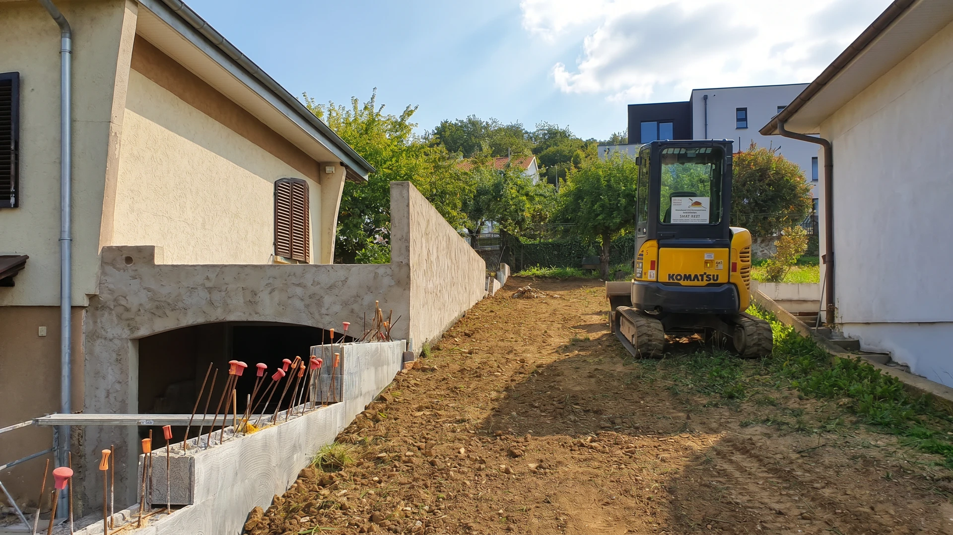 Chantier de construction extérieur avec ouvrier en gilet haute visibilité orange et casque blanc guidant une poutre préfabriquée en béton suspendue par grue