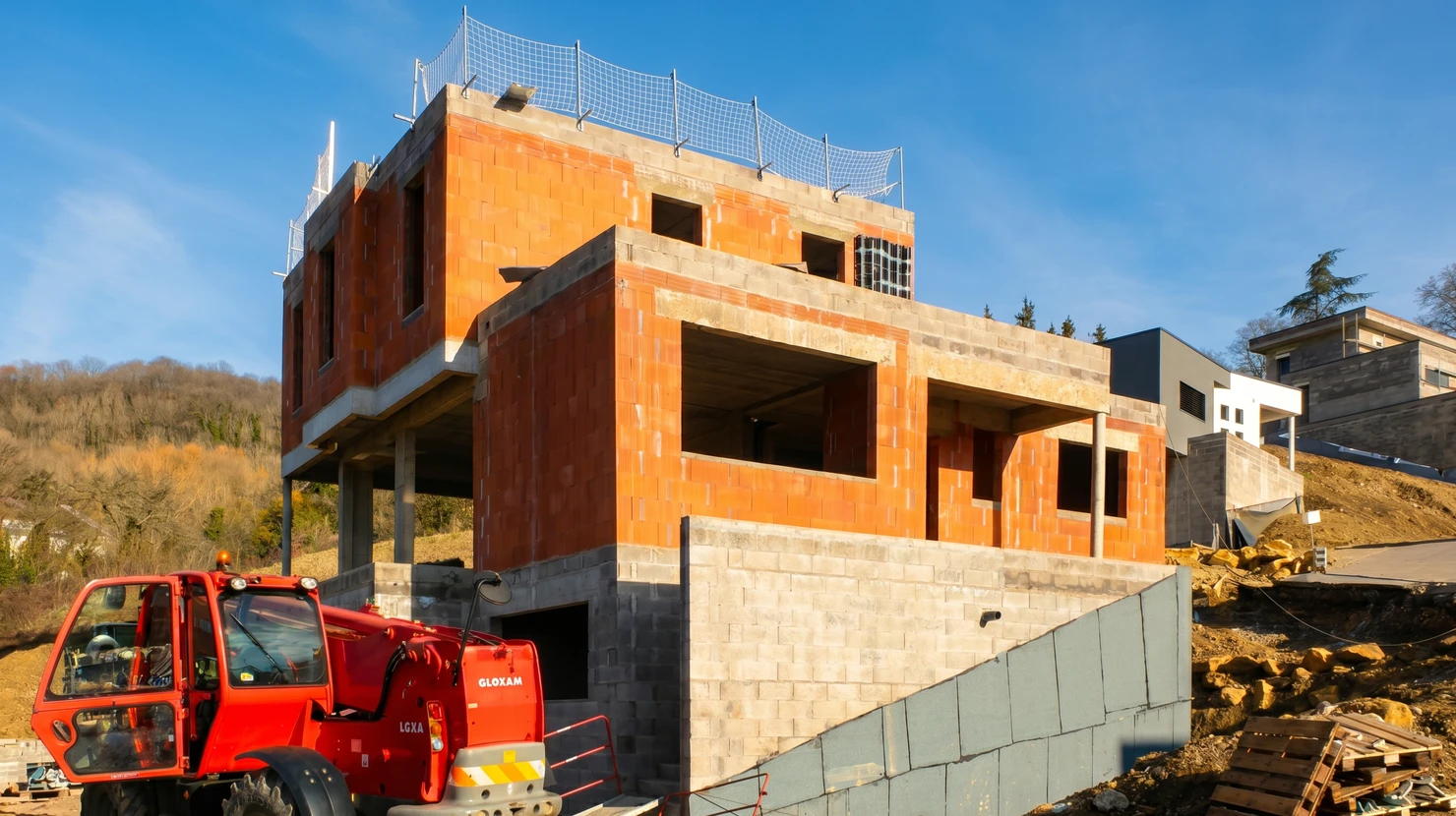 Extension de maison en construction avec murs en blocs de béton, toiture neuve en tuiles grises, échafaudage temporaire