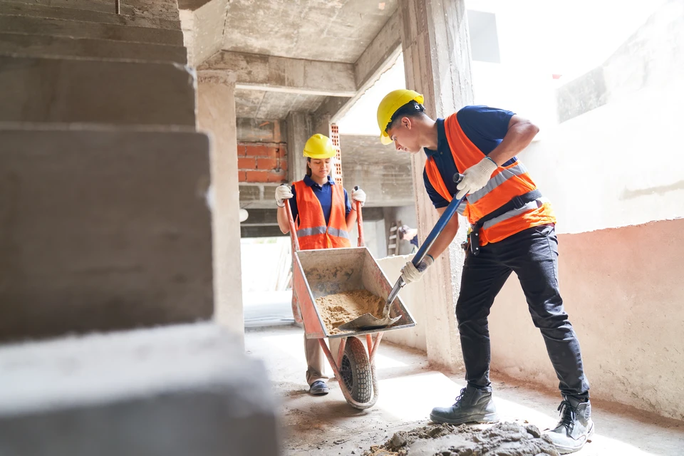 Chantier de construction extérieur avec ouvriers en combinaisons bleues et casques jaunes travaillant sur charpente bois